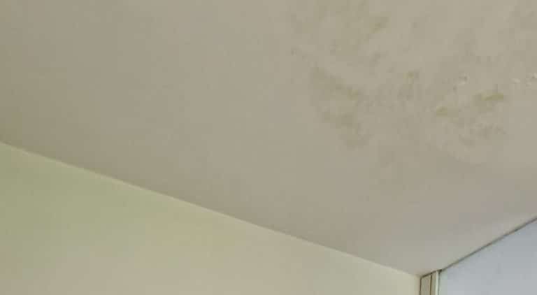 Immagine ravvicinata di un soffitto e muro scrostato, da trattare in fase di ristrutturazione della casa