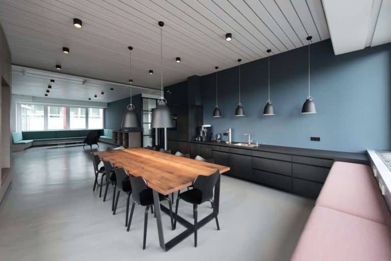 Ampia zona giorno moderna, con cucina scura e minimal, grande tavolo in legno e illuminazione moderna